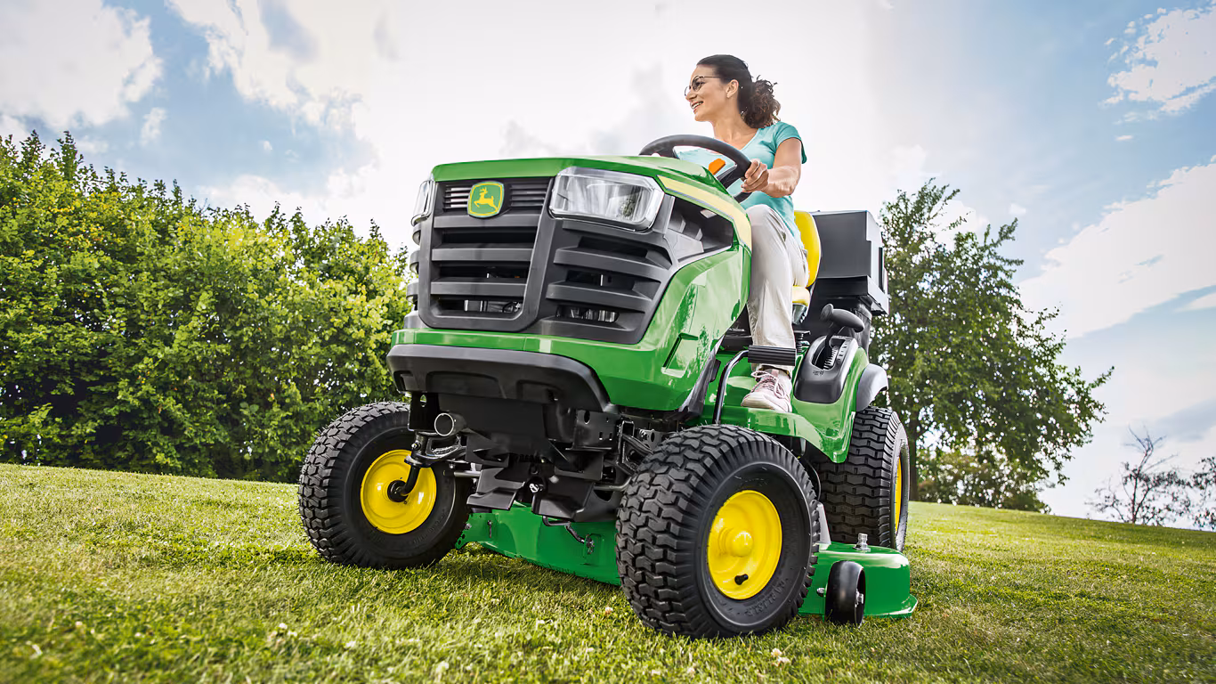 John Deere Garten- und Landschaftspflege-Maschine, Frau sitzt drauf auf dem Rasen